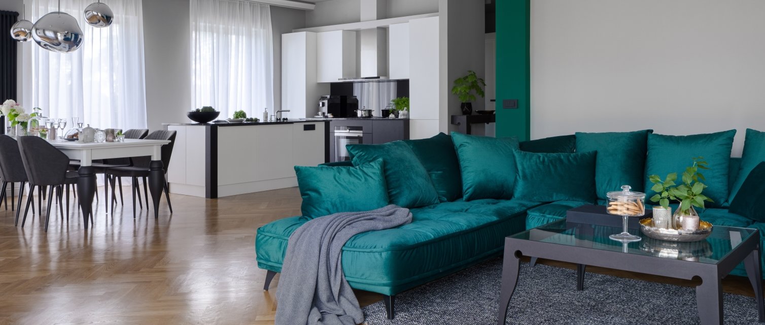 Panorama of spacious apartment with beautiful kitchen with kitchen island and dining table and elegant living room with stylish green corner sofa and modern coffee table